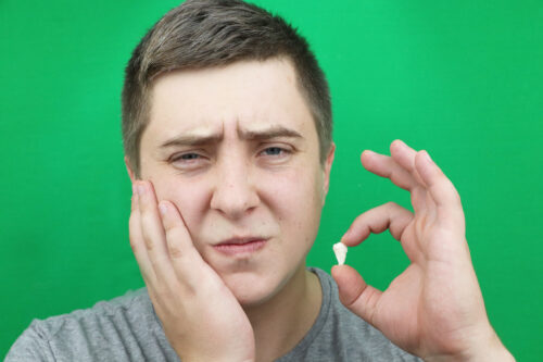 boy holding his face jaw holding wisdom tooth that was extracted