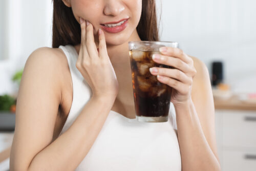 woman holding her face pain in tooth holding up a drink