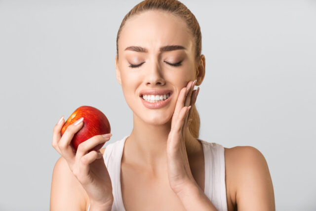 Young Woman Having Tooth Pain Eating Apple On Gray Background