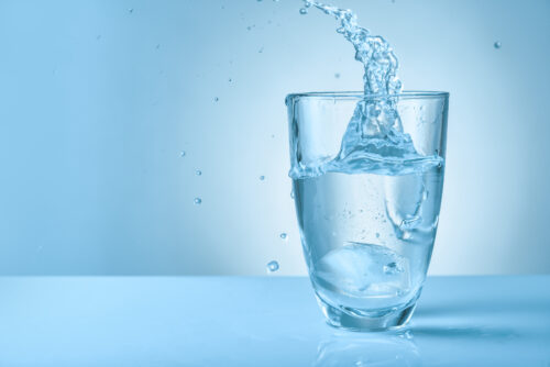 Glass of fresh water with splash on color background