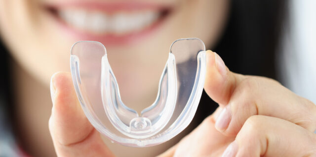Smiling woman holds transparent plastic mouth guard in her hand. Correction of malocclusion and bruxism concept