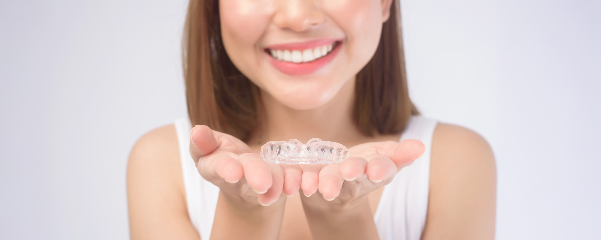 Young smiling woman holding invisalign braces over white background studio