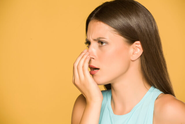 Portrait of beautiful young woman checking her breath on yellow background