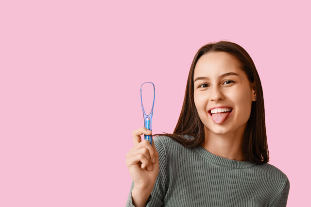 Beautiful young woman with tongue scraper on pink background