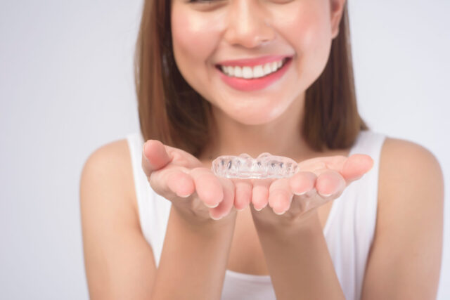 A young smiling woman holding invisalign braces over white background studio, dental healthcare and Orthodontic concept.