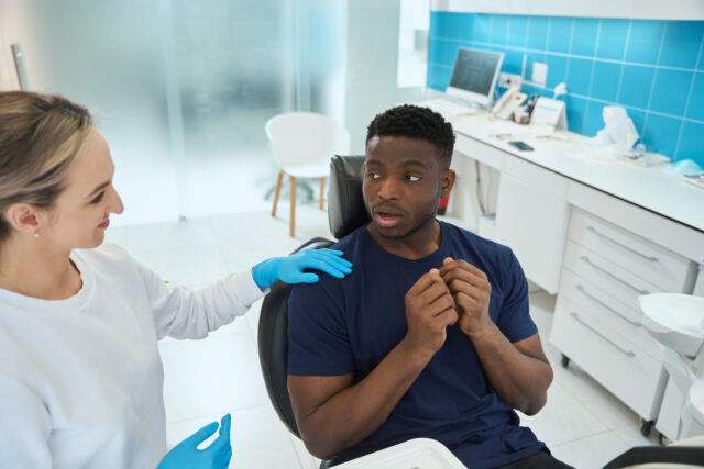 Smiling woman dentist calming down scared young man